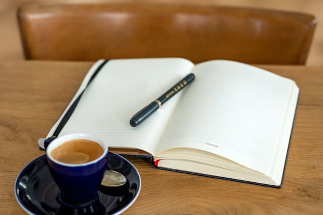 a notebook with a pen and a cup of espresso on a wooden table